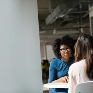 Two women engaged in a discussion in a modern office environment, highlighting communication and interaction.